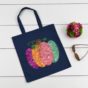 May include: A navy blue tote bag with a colorful sequined pumpkin design. The pumpkin is made of pink, orange, and purple sequins.