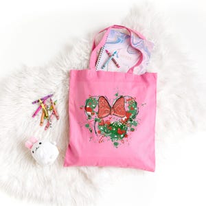 Puede incluir: Bolsa de lona rosa con un gr&aacute;fico verde y rojo de una cabeza de rat&oacute;n de dibujos animados con un lazo. El gr&aacute;fico tiene un efecto de pintura salpicada.