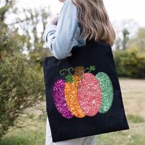 May include: A black tote bag with a sequined pumpkin design. The pumpkin is made of pink, orange, and green sequins.