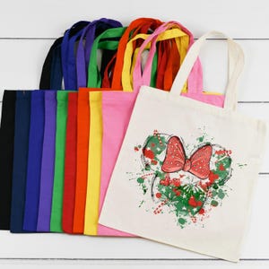 Puede incluir: Un conjunto de 12 bolsas de tela en varios colores, incluyendo negro, azul, morado, verde, rojo, amarillo y rosa. Las bolsas est&aacute;n hechas de lona natural y presentan un dise&ntilde;o impreso de un lazo rojo con lunares blancos y follaje verde.