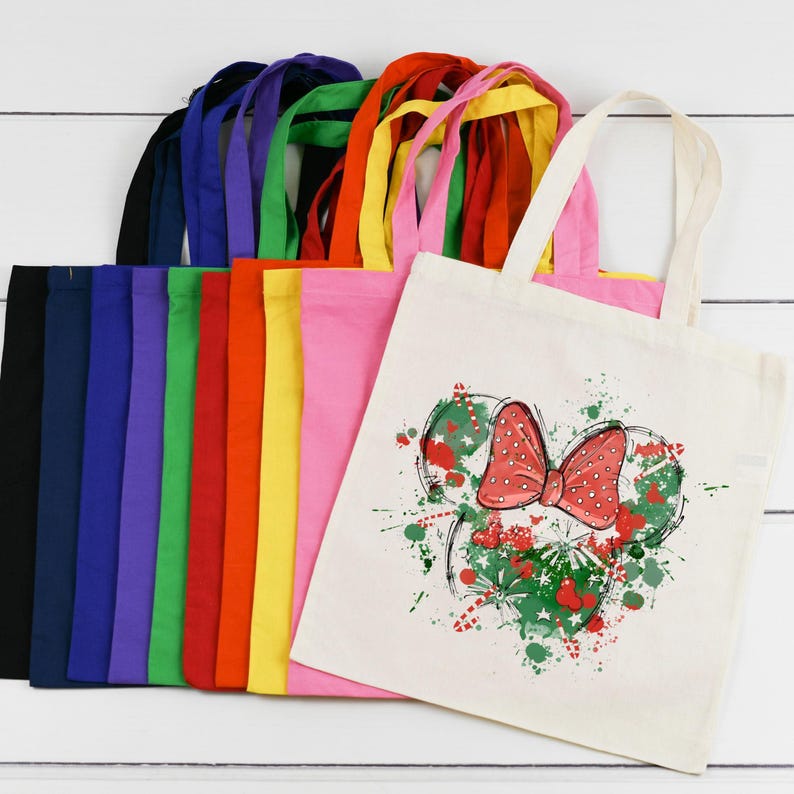 Puede incluir: Un conjunto de 12 bolsas de tela en varios colores, incluyendo negro, azul, morado, verde, rojo, amarillo y rosa. Las bolsas est&aacute;n hechas de lona natural y presentan un dise&ntilde;o impreso de un lazo rojo con lunares blancos y follaje verde.