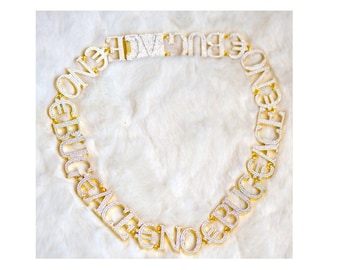 Può includere: Collana a catena d'oro con la parola "BRUGRENCE" scritta in grandi lettere incastonate con diamanti.