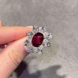 Puede incluir: Un anillo de rubí rojo con una montura en forma de flor engastada con pequeños diamantes blancos.