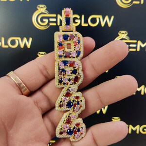 May include: Gold pendant with the letters "1942" set with colorful gemstones, including red, blue, and pink.