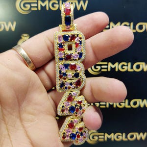 May include: Gold pendant necklace with the letters "1944" spelled out in gold and set with red, blue, and pink gemstones.