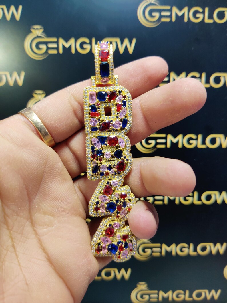 May include: Gold pendant necklace with the letters "1944" spelled out in gold and set with red, blue, and pink gemstones.