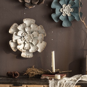 May include: Three metal wall decor flowers in different colors and sizes. The flowers are in shades of brown, blue, and white. The flowers are made of metal and have a distressed finish.