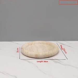May include: A beige, oval-shaped decorative tray. The tray is 20 cm long, 20 cm wide, and 3 cm thick. The tray has a textured surface and is made of a light-colored material.