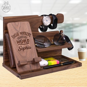 May include: A wooden desktop organizer with a phone stand, watch holder, sunglasses holder, and a tray for keys and other small items. The organizer is engraved with the text "Social Workers Change the World Sophia".