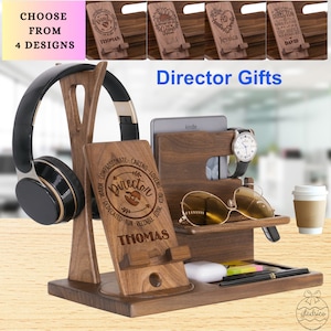 May include: A wooden desk organizer with a personalized inscription that reads "Warm, Compassionate, Caring, Loving, Dedicated, Fun, Reliable, Quick, Loyal, Director, Thomas". The organizer has slots for a phone, watch, sunglasses, and a cup. It also includes a headphone stand and a small shelf for a book or tablet.