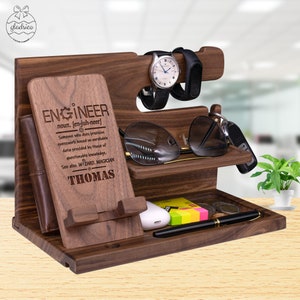 May include: A wooden organizer with a phone stand, watch holder, glasses holder, key holder, and a pen holder. The organizer is engraved with the word "Engineer" and a definition. The name "Thomas" is also engraved on the organizer.