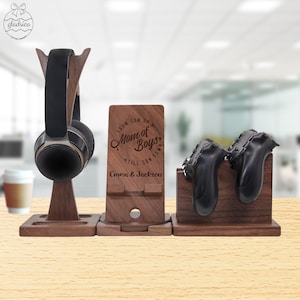 May include: A wooden stand with three compartments for organizing gaming accessories. The stand has a phone holder, a headphone holder, and a holder for two controllers. The stand is engraved with the text "From Son Up, Mom of Boys, Till Son Down, Emma & Jackson".