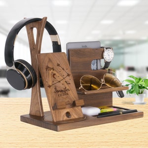 May include: A wooden desk organizer with multiple compartments. It features a headphone stand, a phone holder with the text "Aries Jennifer 4.10.2005", a tablet slot, a watch holder, a sunglasses shelf, and a tray for small items. The organizer is made of dark wood.