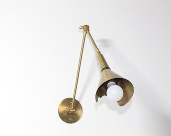 May include: A brass wall sconce with a cone-shaped shade and a single light bulb. The sconce has a long, adjustable arm.