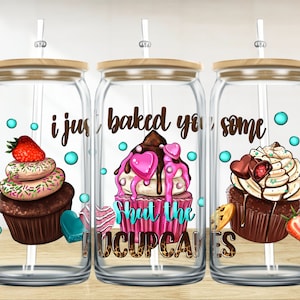 May include: Three glass mason jars with wooden lids and straws. Each jar has a different cupcake design and text. The first jar says "i just baked you some". The second jar says "Shut the cupcakes". The third jar has a cupcake with a pink heart and chocolate drizzle.