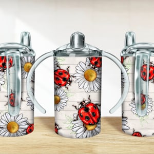 May include: Three clear plastic cups with handles and lids. The cups have a white background with a pattern of red ladybugs and white daisies.