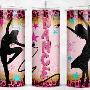 Puede incluir: Un vaso rosa y dorado con una silueta de una bailarina y la palabra "DANCE" en letras de purpurina rosa. El fondo presenta un estampado de leopardo y estrellas.