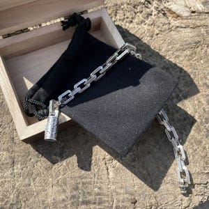 May include: A silver chain bracelet with a decorative clasp and a matching chain section, displayed on a black velvet pouch inside an open wooden box. The bracelet is resting on a wooden surface.
