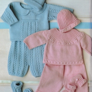Puede incluir: Dos conjuntos de ropa de bebé de punto en azul claro y rosa. Cada conjunto incluye un suéter, pantalones, gorro y patucos. El conjunto azul tiene un suéter con cuello y detalles de punto trenzado. El conjunto rosa presenta un suéter de cuello redondo con un ribete decorativo.