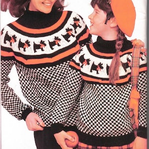 Puede incluir: Un suéter de punto blanco y negro con un patrón de pata de gallo blanco y negro y un yugo estampado en negro, naranja y blanco con perros negros. El suéter tiene cuello alto y mangas largas. La modelo lleva una falda de cuadros rojos y negros.