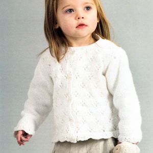 May include: A white knitted cardigan with a delicate lace pattern and button closure. The cardigan has a round neckline and long sleeves.