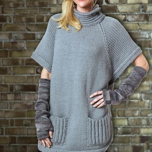 Puede incluir: Una túnica de punto gris con cuello alto y mangas cortas. La túnica tiene dos bolsillos delanteros y se combina con guantes sin dedos grises a juego. La modelo lleva pantalones negros.