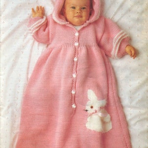 May include: A pink knitted baby gown with a white bunny applique and white trim. The gown has a hood and buttons down the front.