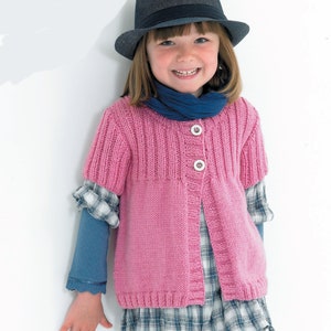 May include: A pink knitted cardigan with a button closure and short sleeves. The cardigan is worn over a plaid shirt and a blue scarf. The person is wearing a black fedora.