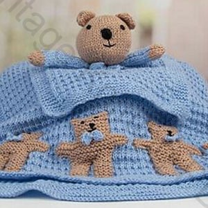 Könnte beinhalten: Eine blaue gestrickte Babydecke mit einem braunen Teddybär und drei kleineren Teddybären. Die Decke hat Bommeln an den Rändern.