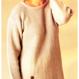 May include: A light beige, long-sleeved sweater with a textured knit pattern. The sweater has a round neckline and two brown buttons on the side. The garment is a tunic style.
