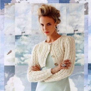 May include: A white knitted cropped cardigan with a cable knit pattern and button closure. The cardigan is worn over a light blue dress.