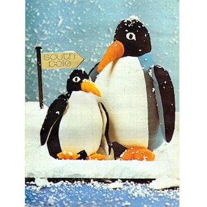 Puede incluir: Dos figuras de pingüinos con cabezas, alas y espaldas negras, vientres blancos y picos y pies naranjas, de pie en una escena nevada. Un letrero dice "Polo Sur". El fondo es azul claro con copos blancos.