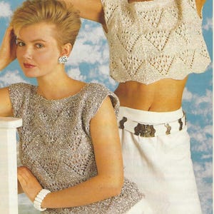 Op de afbeelding: Twee vrouwen dragen gebreide tops. De ene is lichtbeige, de andere lichtgrijs. Beide tops hebben een geometrisch open patroon. Eén vrouw draagt een witte armband, de ander een witte riem met een decoratieve gesp.