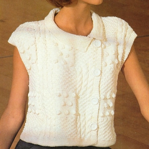 Könnte beinhalten: Eine weiße, ärmellose Strickjacke mit Kragen, Knopfleiste und Zopfmuster. Die Strickjacke hat ein strukturiertes Design mit kleinen, erhabenen Punkten.