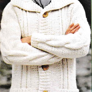 May include: Cream-colored cable-knit cardigan sweater with a shawl collar and large wooden buttons. The sweater has two front pockets and is worn with a gray scarf. A classic, warm garment.