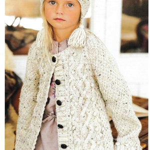 May include: A white knitted cardigan with a cable knit pattern and a pom-pom on the hat. The cardigan has a button closure and is worn over a white shirt and blue jeans. The text "Clancy Helmet p51 Twig Cardie p61" is visible at the bottom of the image.
