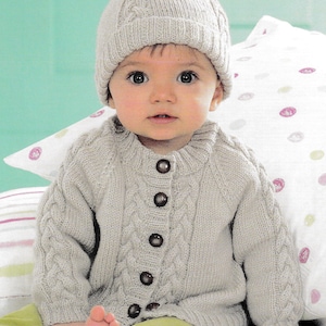 May include: A baby wearing a gray knitted cardigan with buttons and a matching gray knitted hat with a pompom on top.