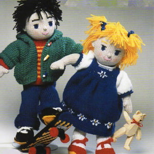 Peut inclure: Deux poupées en tricot, l'une avec des cheveux noirs et une veste verte, l'autre avec des cheveux blonds et une robe bleue, debout ensemble. La poupée aux cheveux noirs tient une planche à roulettes.