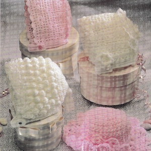 May include: Four handmade baby bonnets and a sun hat in soft pastel colours. The bonnets are in white and pink, with delicate crochet patterns and decorative details. The sun hat has a wide, ruffled brim.