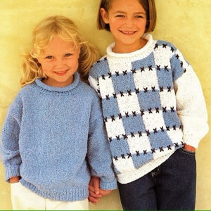 May include: Two children wearing blue and white knit sweaters. The girl on the left is wearing a solid blue sweater. The girl on the right is wearing a sweater with a checkered pattern in blue and white with black accents.