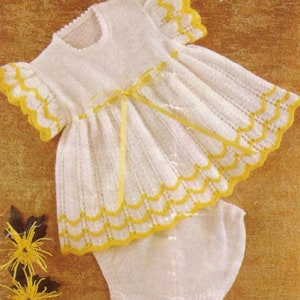 May include: A white knitted baby dress with yellow trim and a matching knitted diaper. The dress has a ruffled neckline and a bow at the waist.
