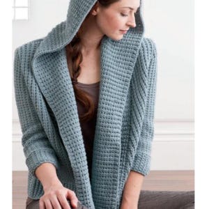 Könnte beinhalten: Ein hellblauer Kapuzenpullover mit lockerer Passform. Der Pullover ist mit einem strukturierten Stichmuster gestrickt.