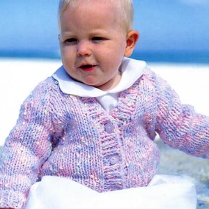 May include: A baby wearing a pink and purple knitted cardigan with a white collar and buttons. The cardigan has a speckled pattern.