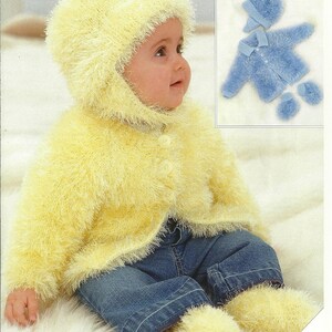 Op de afbeelding: Een gele gebreide baby-cardigan met een capuchon en bijpassende slofjes. De cardigan heeft een pluche textuur en wordt aan de voorkant dichtgeknoopt. De slofjes hebben pompoentjes aan de bovenkant.