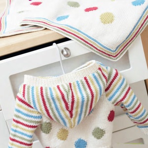 May include: A white knitted baby sweater with a striped hood and colorful polka dots. The sweater is hanging on a white dresser drawer.
