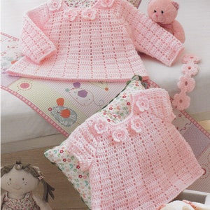 Puede incluir: Dos jerséis de bebé de color rosa hechos a crochet con detalles de flores. Los jerséis están hechos con un punto delicado y tienen un diseño femenino.