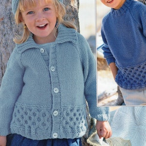 May include: Two children wearing blue knitted cardigans with button fastenings and a lace-like trim. The cardigan on the left has a collar. Both cardigans are a light blue colour.