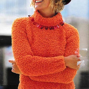Può includere: Un maglione arancione brillante a collo alto con una collana di perline decorative. Il maglione ha una texture soffice.
