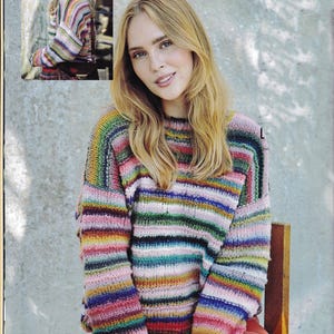 May include: A colorful, striped sweater with a round neckline. The sweater features horizontal stripes in various colors, including pink, green, blue, and yellow. The sleeves are long, and the sweater appears to be made of a soft, knitted material. The model is wearing the sweater.