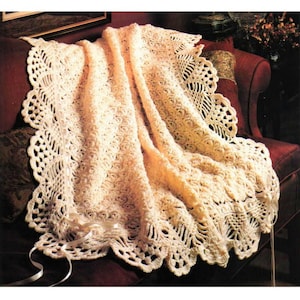 May include: A cream-colored, crocheted blanket with a scalloped edge and intricate openwork patterns. The blanket is draped over a red armchair, with a satin ribbon detail. The handmade blanket is a cozy home decor item.